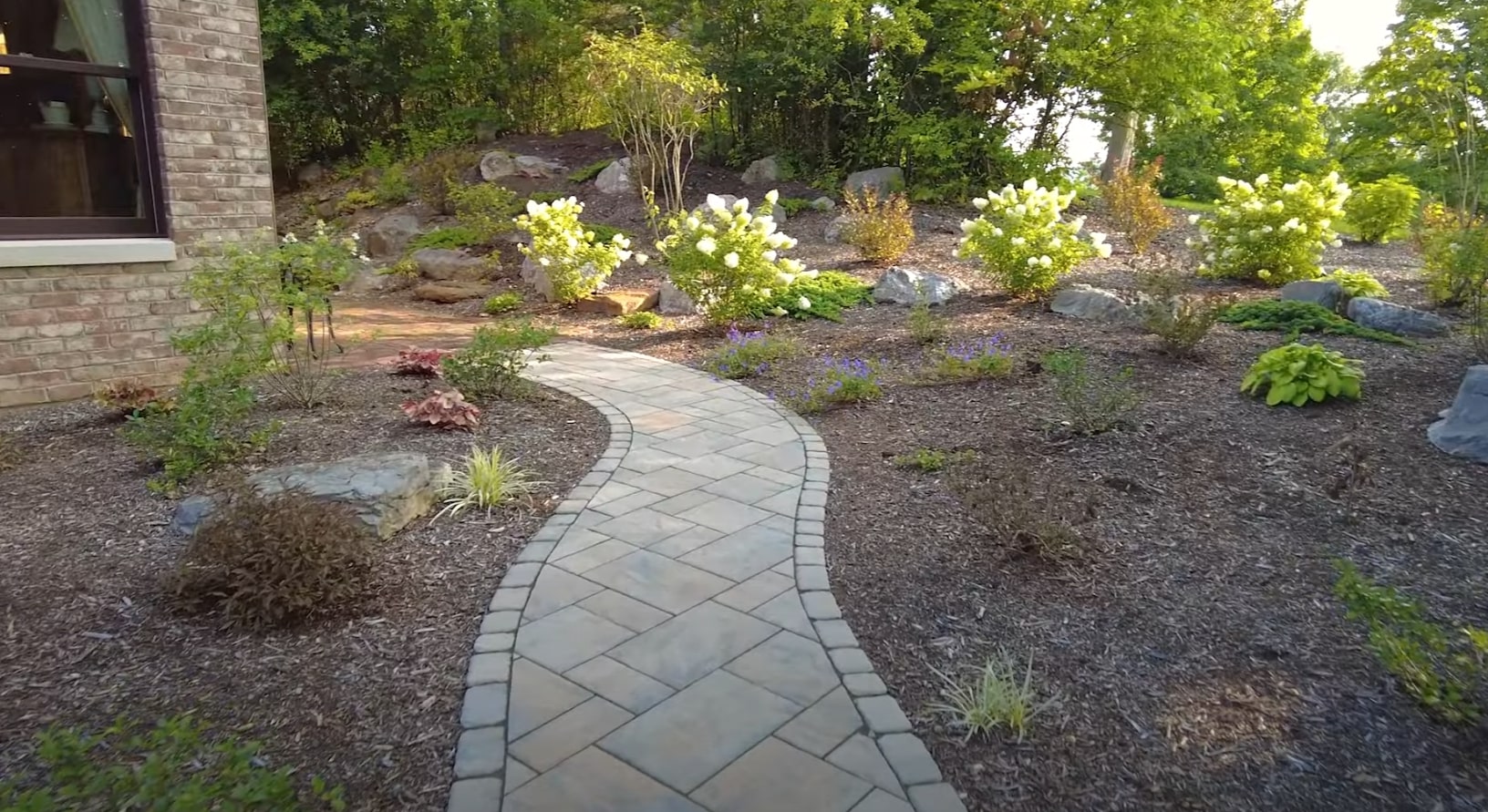 Professional landscape design featuring curved stone walkway and seasonal plantings Curved stone pathway through landscaped garden with mature shrubs and decorative plantings