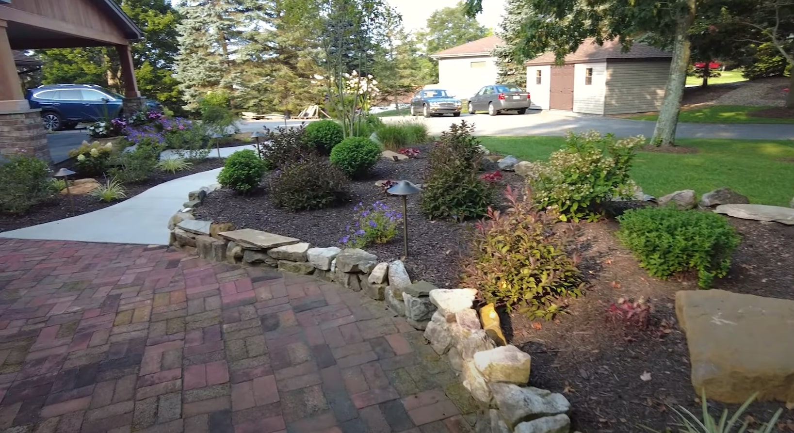 Professional landscape design incorporating lighting-ready hardscaping and plant arrangements Front yard landscape with natural stone features, decorative plantings, and brick paver pathways