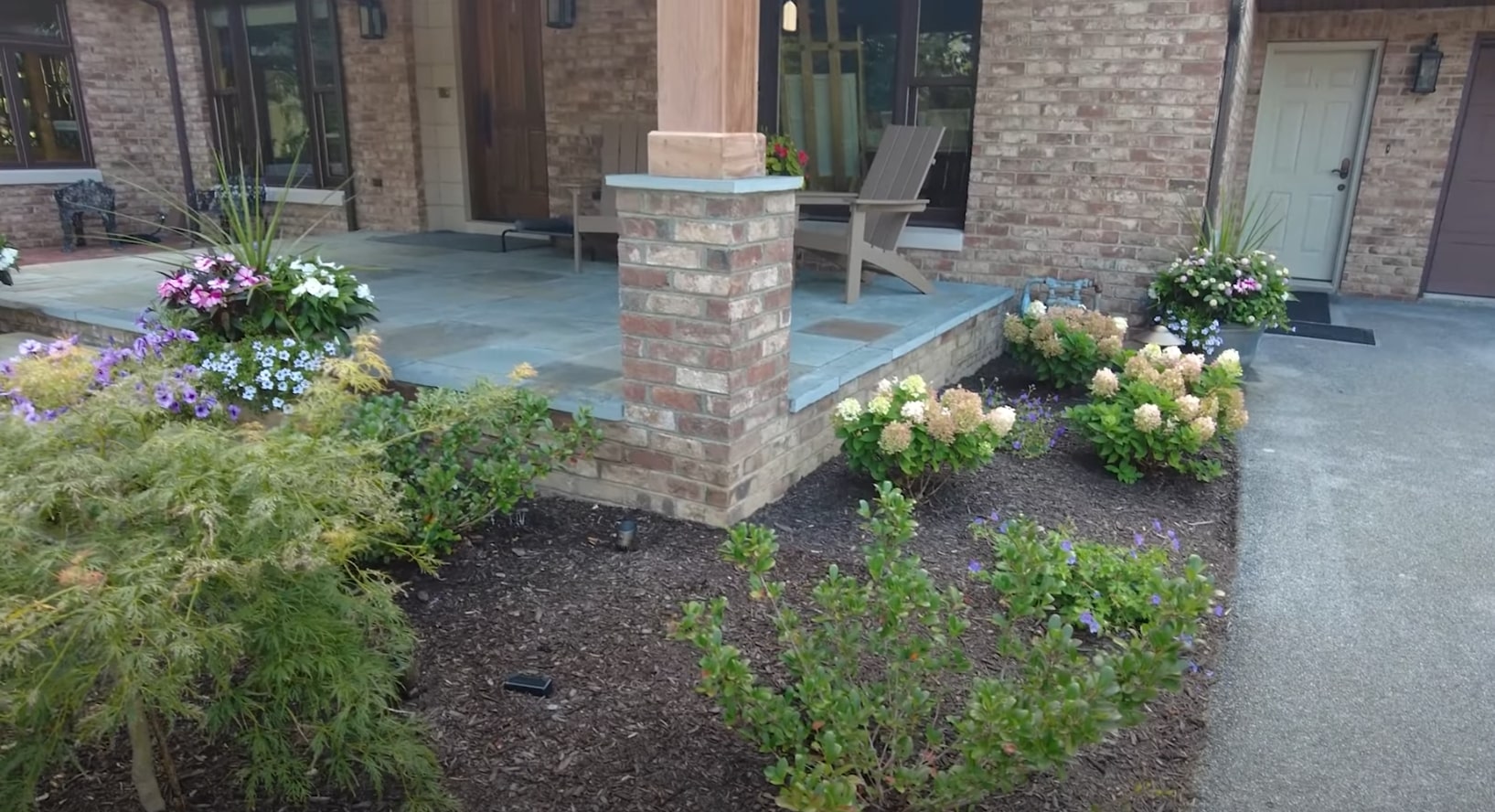 Front entrance landscaping with brick hardscaping and colorful seasonal displays Residential front entry with professional landscaping, brick features, and seasonal plantings